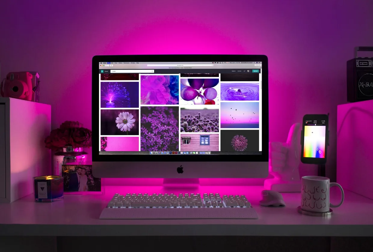 Mesa com um monitor mostrando uma grade de imagens sob luz rosa